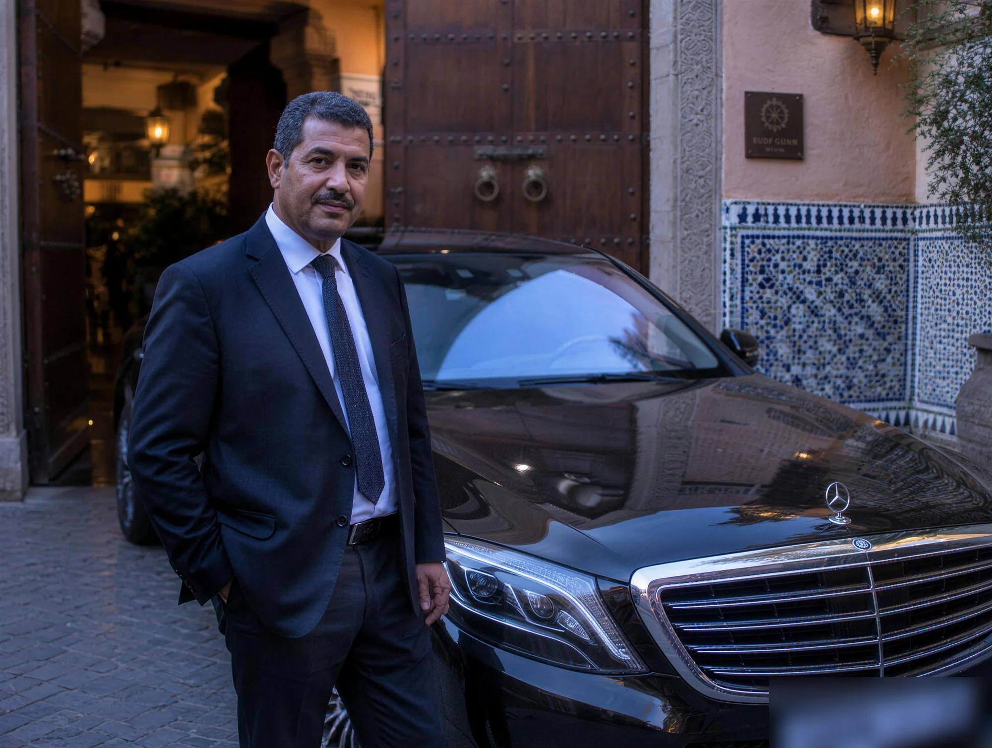 S3S chauffeur beside a black Mercedes-Benz S-Class at a Marrakech hotel entrance at dusk